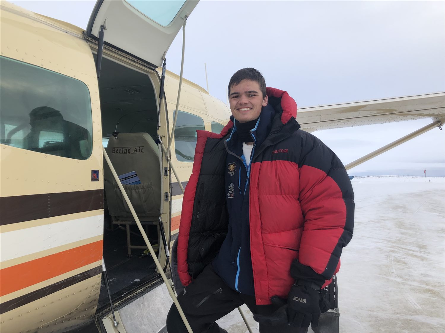 Caden grinning beside a Bering Air Cessna on a snowy Alaska airstrip