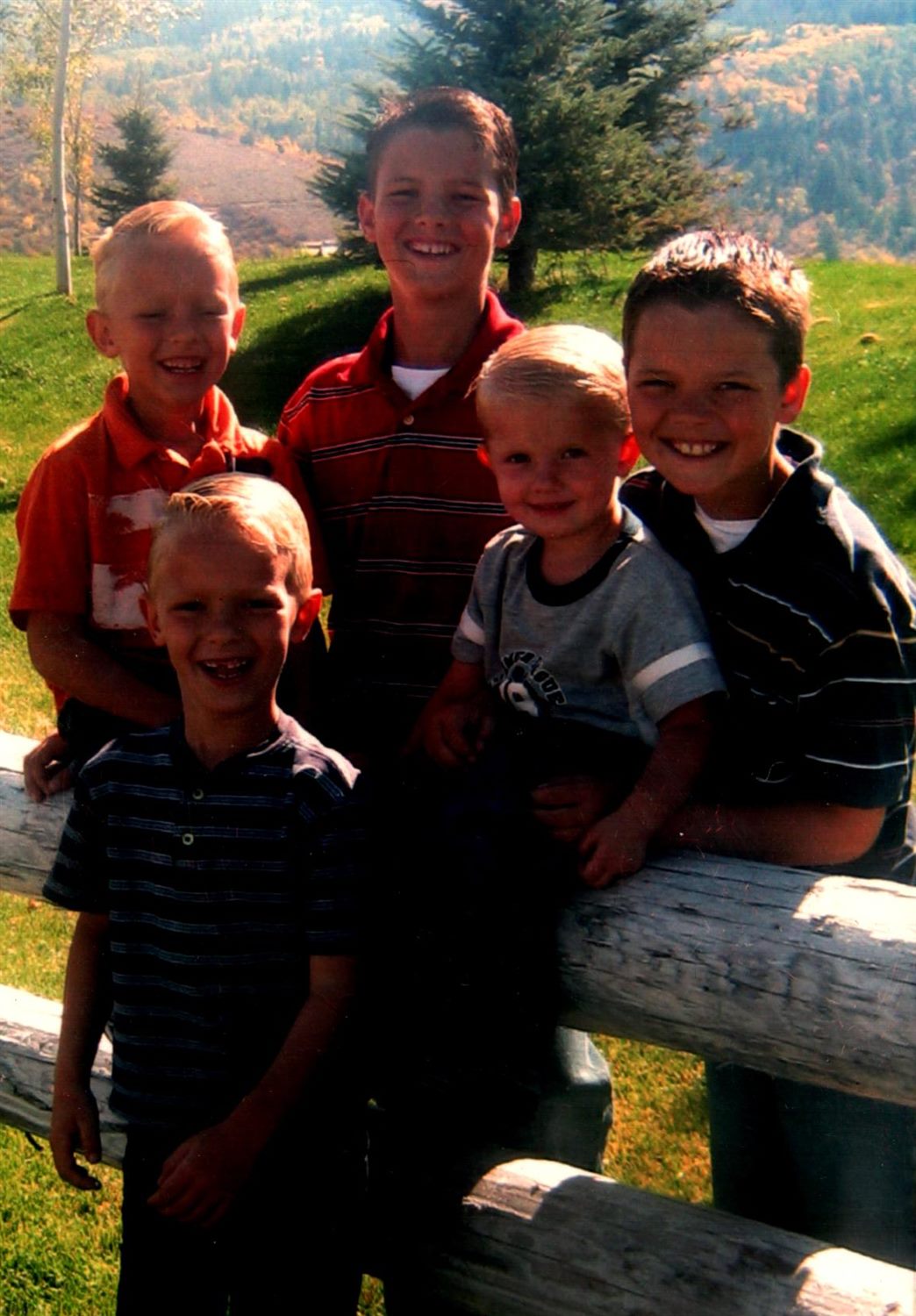 All five West brothers laughing together on a log fence in a mountain valley