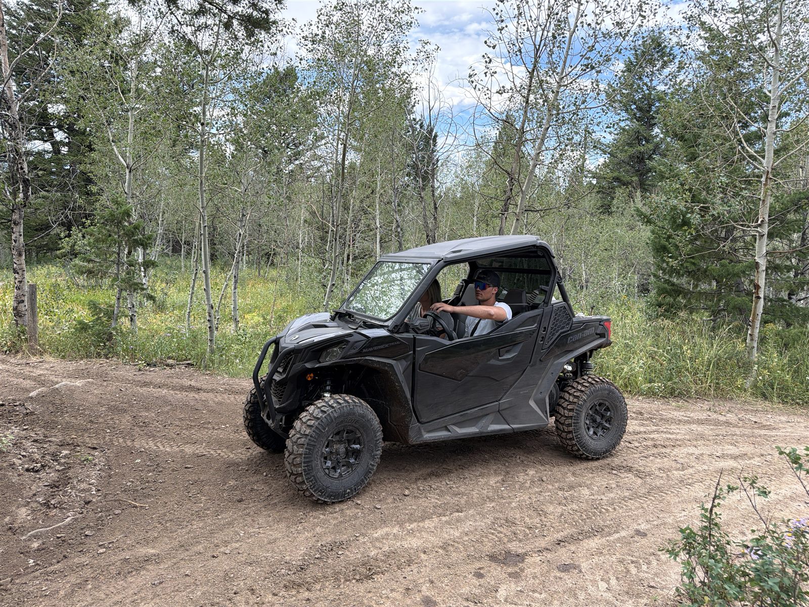 Caden driving a Can-Am side-by-side on an aspen-lined dirt trail