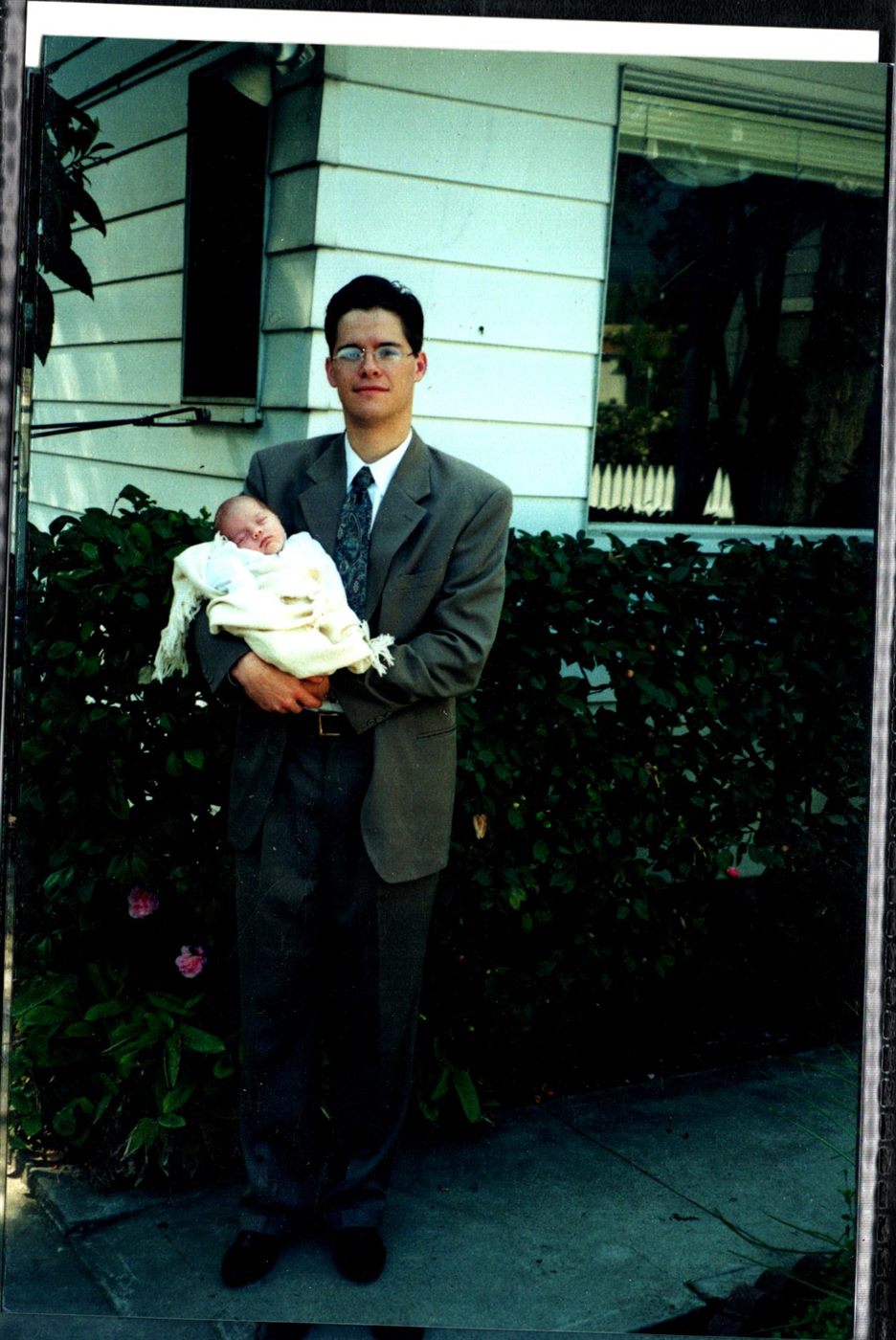 Young Jason in a suit holding baby Caden wrapped in white
