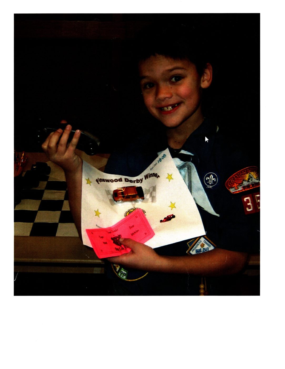 Caden in Cub Scout uniform proudly holding his Pinewood Derby car and winner certificate
