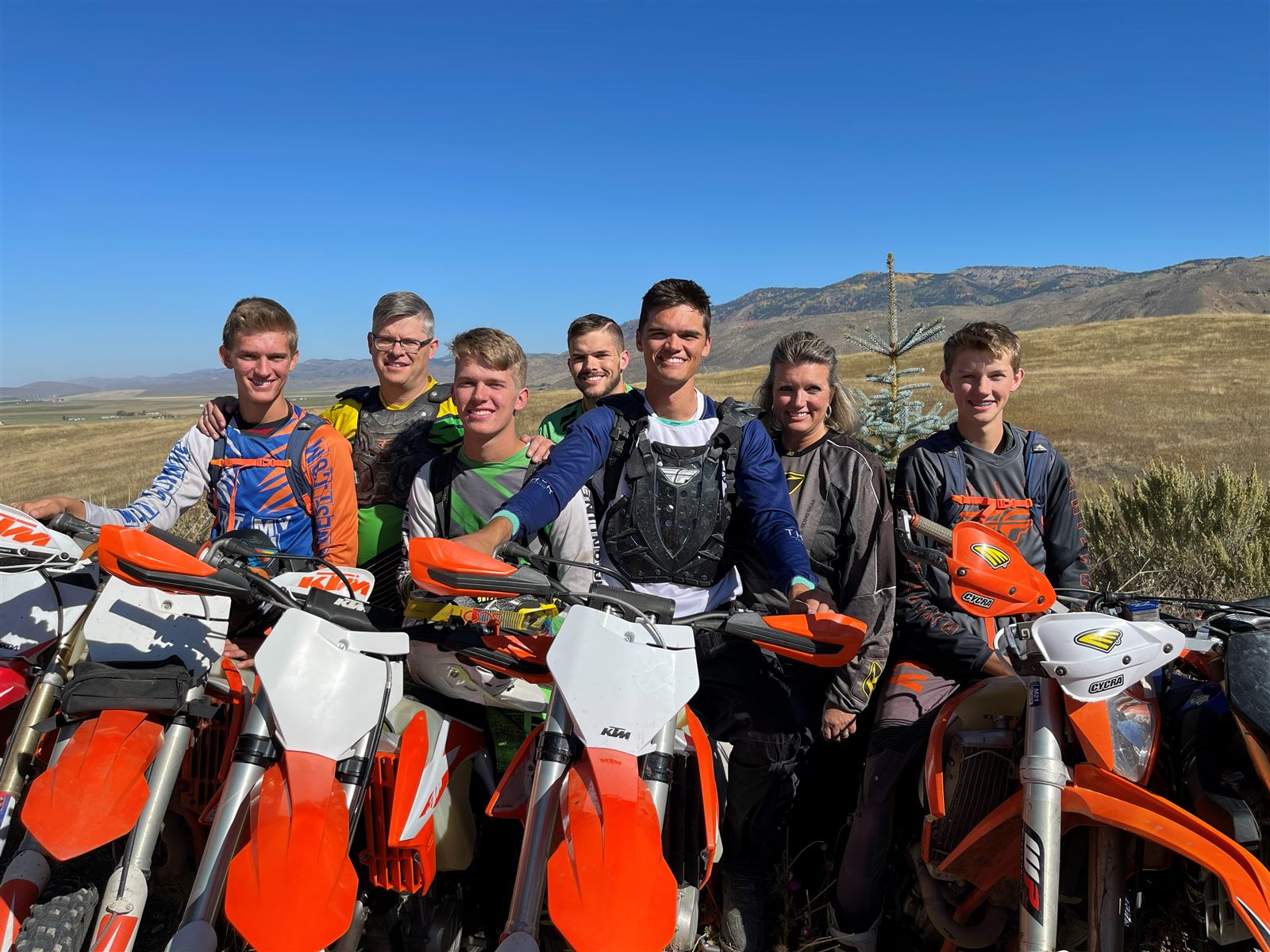 The whole West family in motocross gear with their dirt bikes in a mountain valley