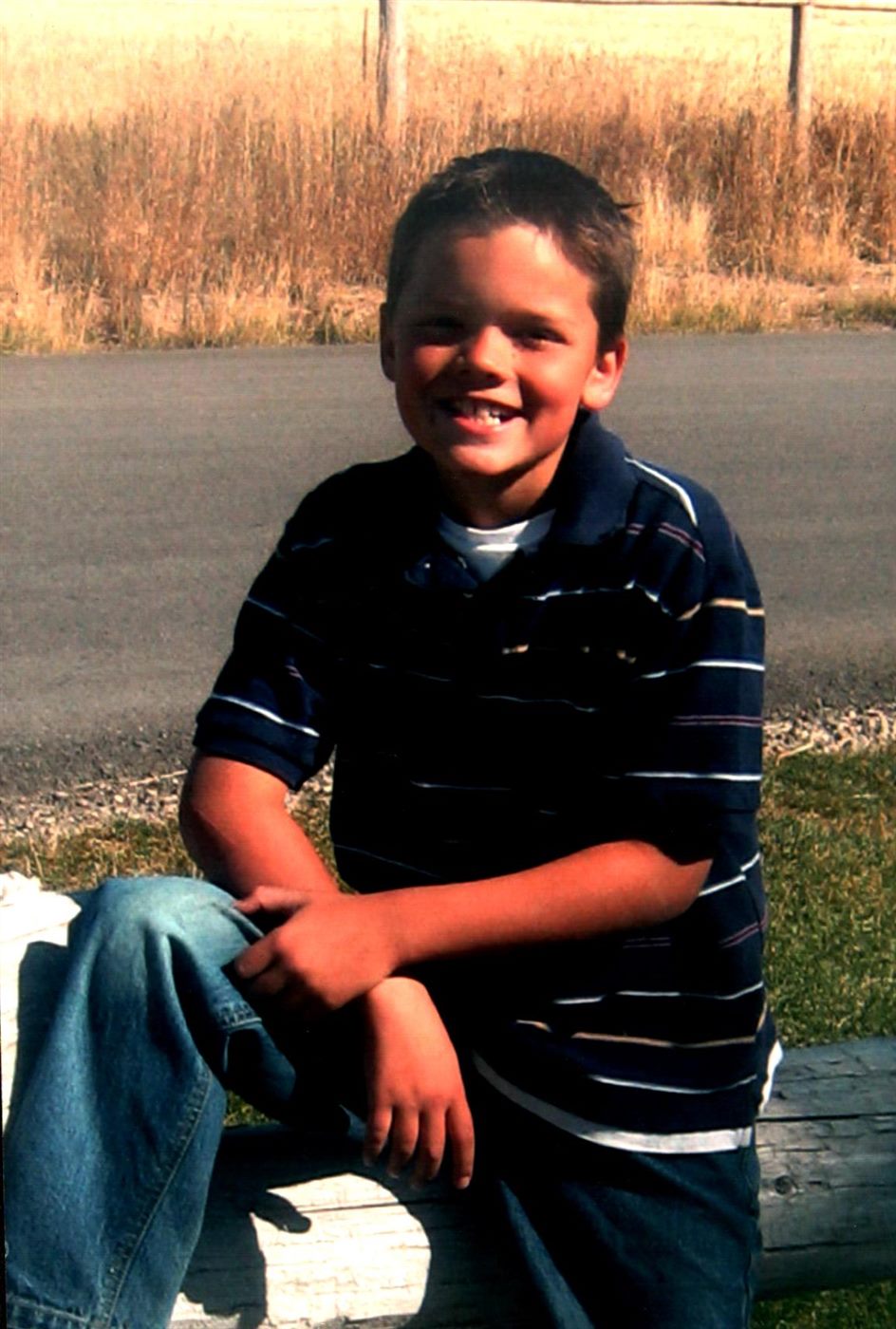 Young Caden smiling on a wooden fence rail beside a country road