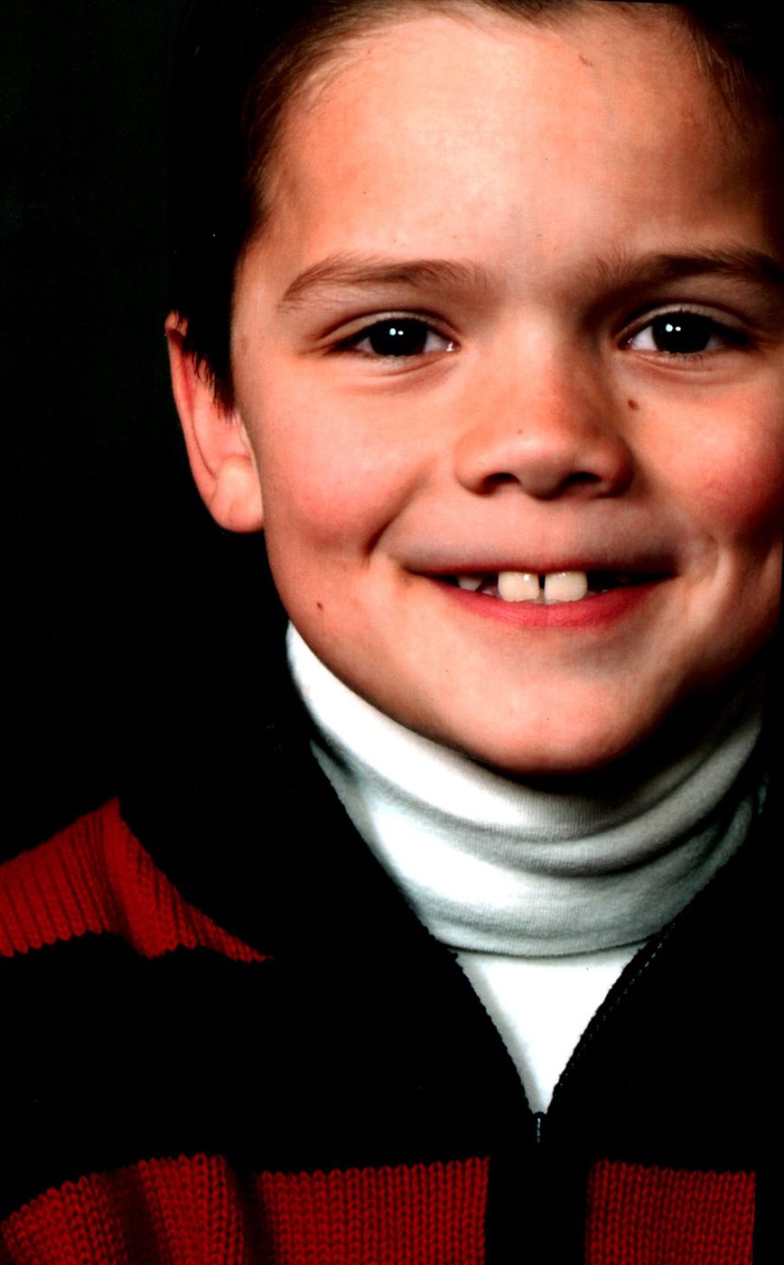 Close-up of young Caden with a gap-toothed smile in a red and black sweater