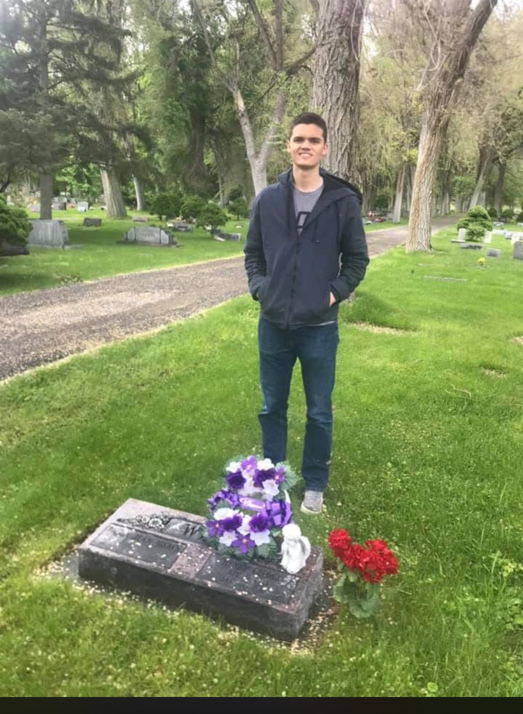 Caden standing at his grandfather's grave with purple and red flowers