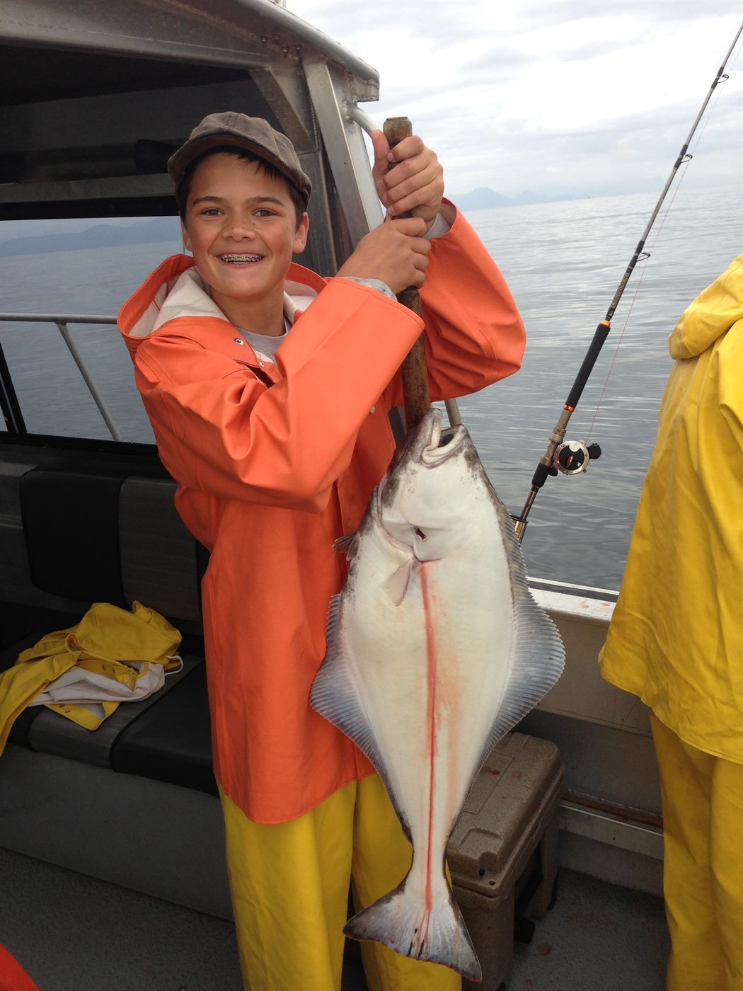 Young Caden in orange rain gear holding a huge halibut on a boat