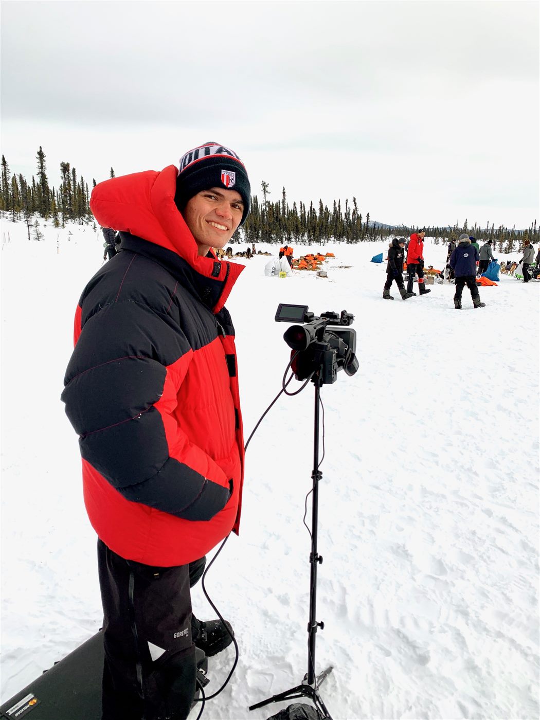 Caden in a red parka filming the Iditarod with a professional camera in the snow