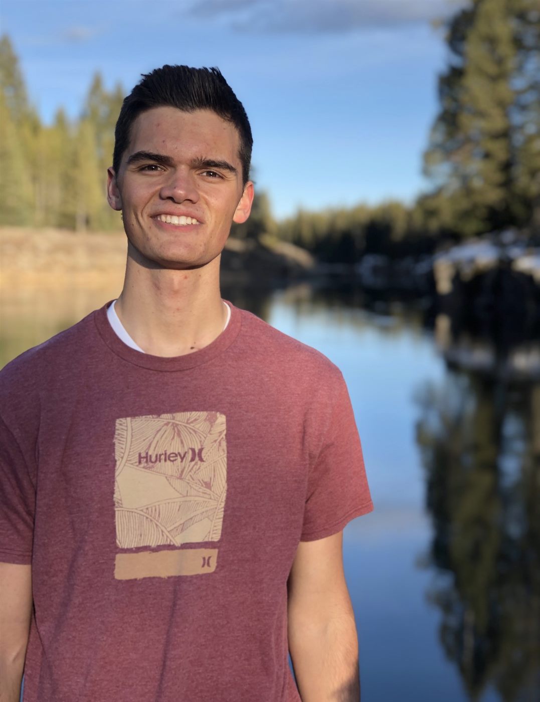 Caden smiling at a still mountain lake in golden evening light
