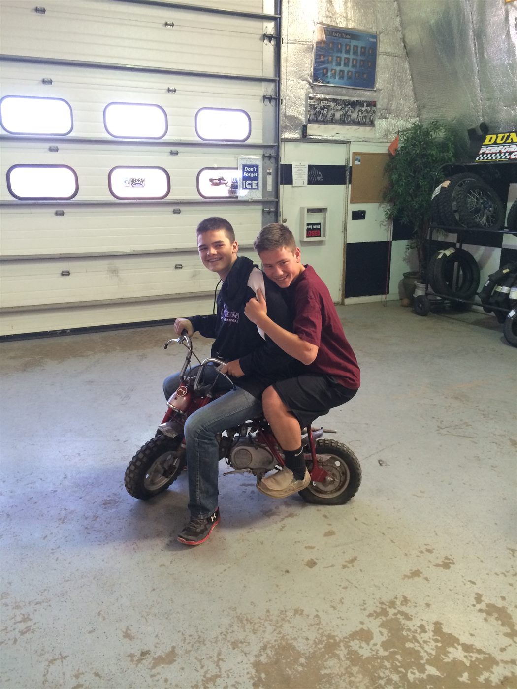 Two brothers sharing a tiny red mini bike inside a motorcycle shop