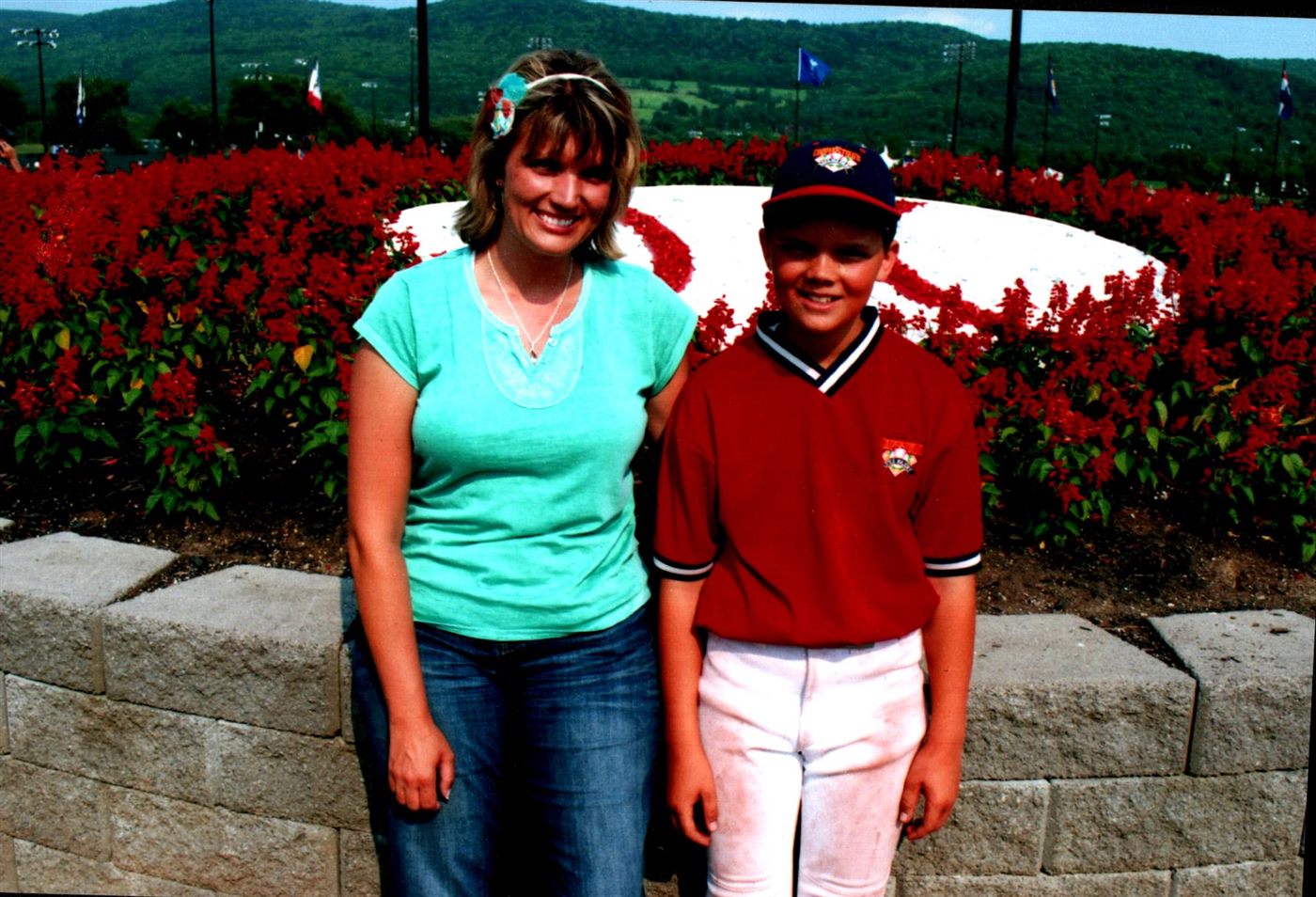 Caden in a red Cooperstown jersey beside his mom in front of red flowers