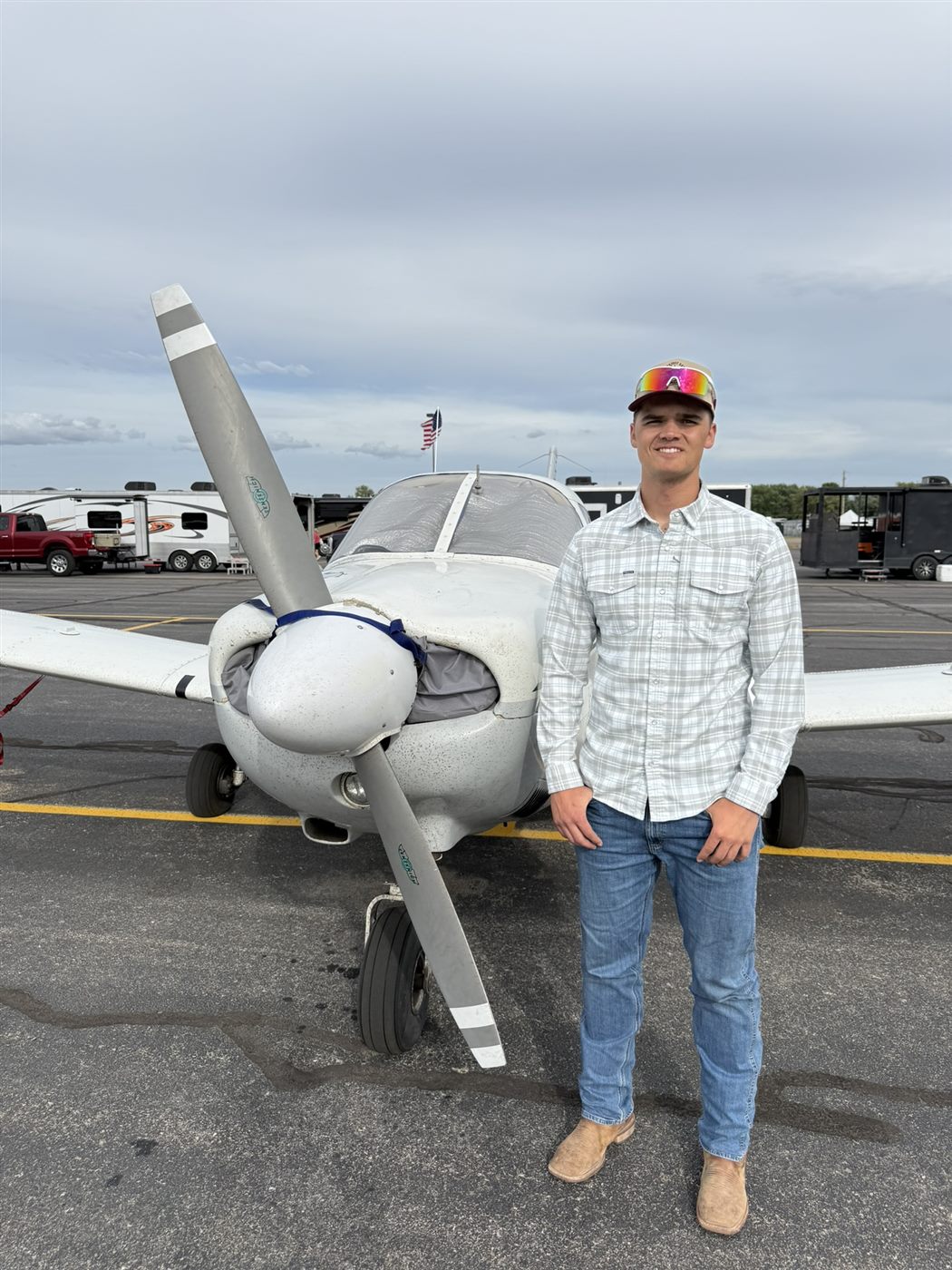 Caden standing proudly beside his white airplane at the airfield