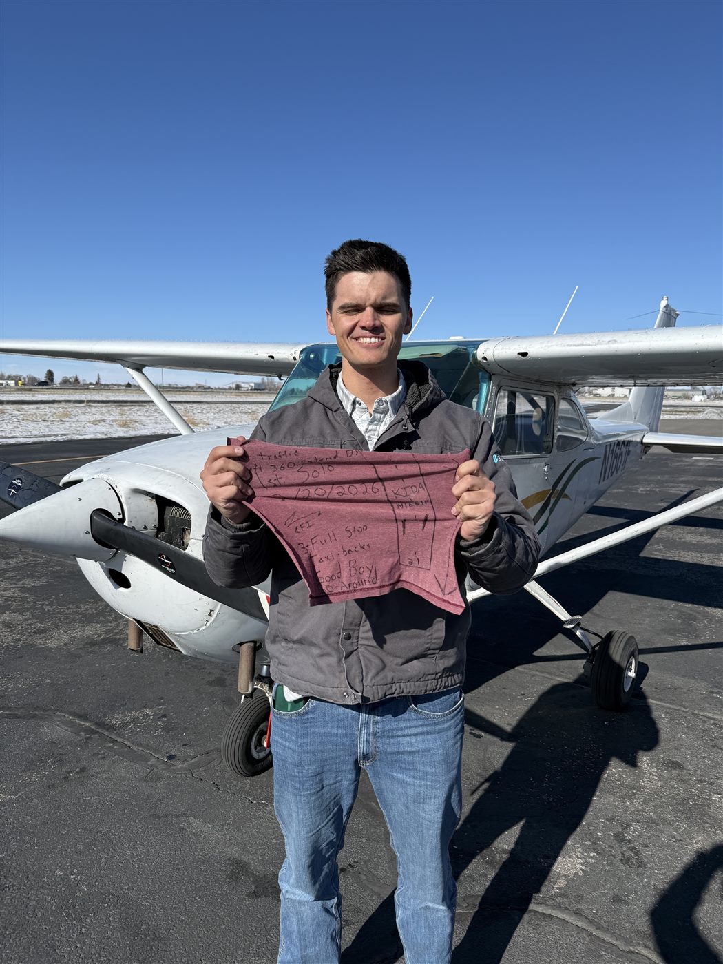 Caden beside a Cessna holding the inscribed shirt-tail from his milestone flight