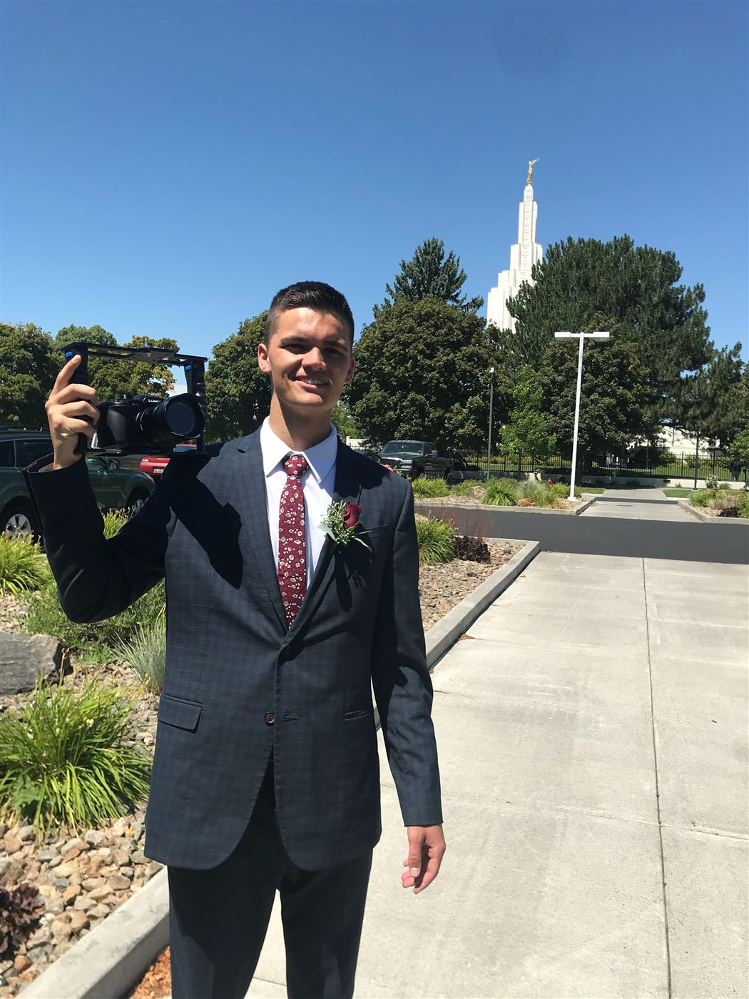 Caden in a suit holding a camera with a temple spire behind him