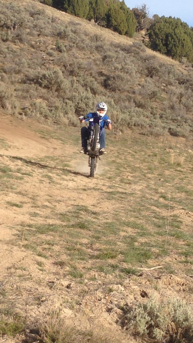 A boy riding a wheelie on a dirt bike up a desert trail